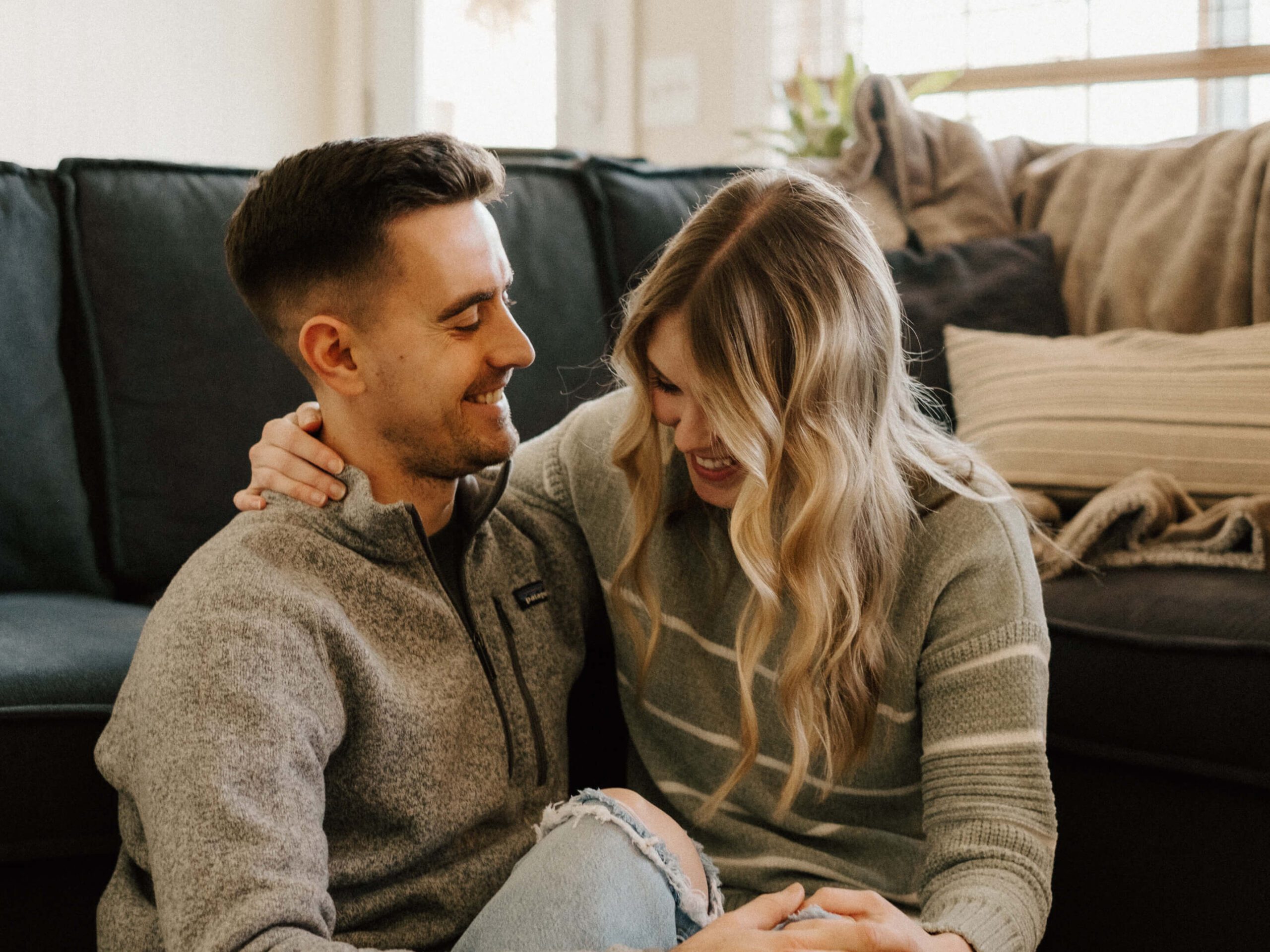 A couple laughing in a relaxed pose on their living room floor, in a documentary style in-home photoshoot by Stacey Vandas Photography.