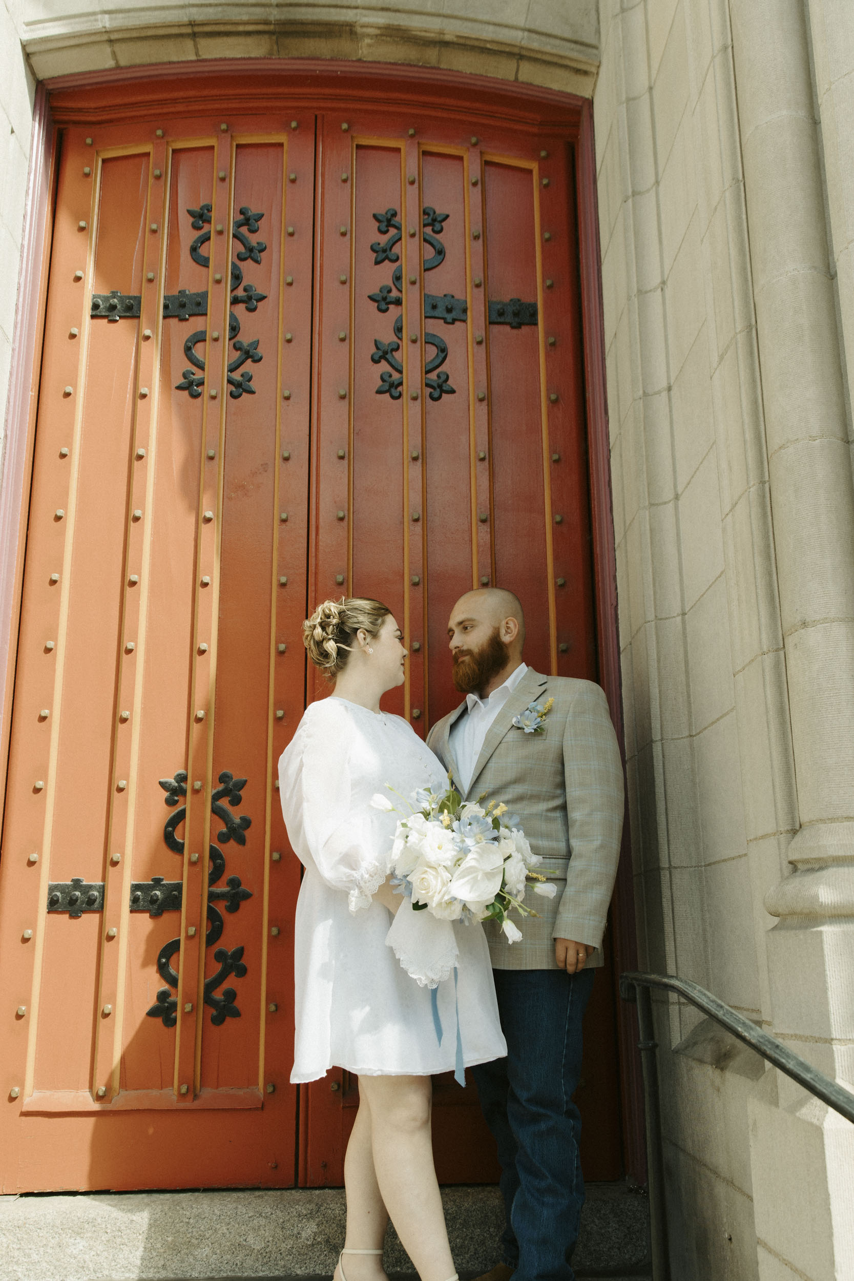 A couple poses in front of a red church door during a casual St. Louis elopement.