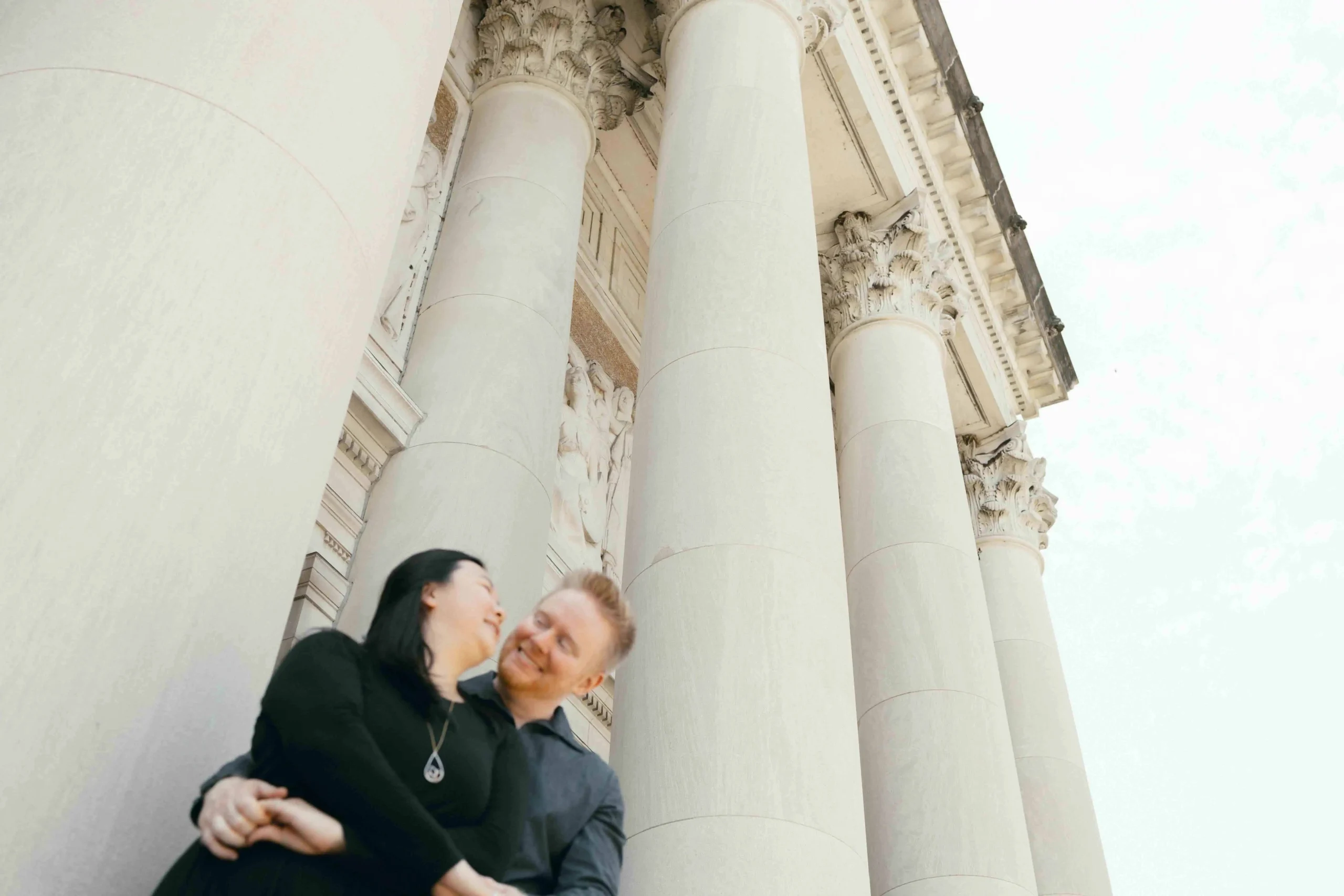 A couple smiling and embracing in front of a museum with Greek columns in St. Louis, Missouri.