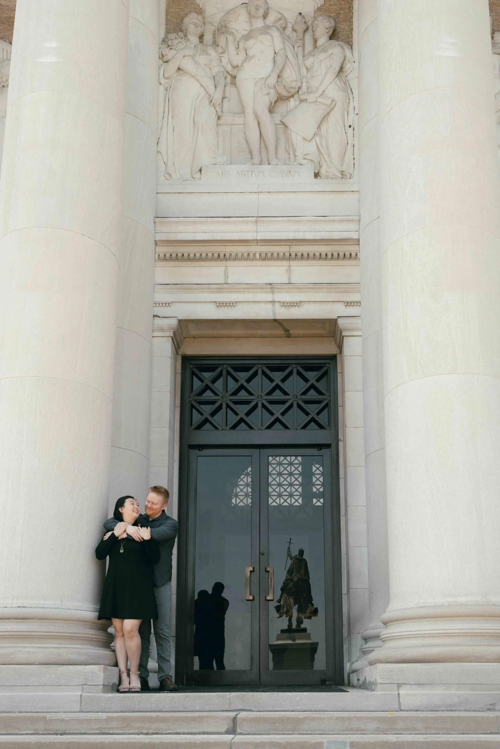 A couple embracing in front of a historic art museum in Saint Louis, Missouri with Greek-style columns, shot by Stacey Vandas with a nostalgic film style.