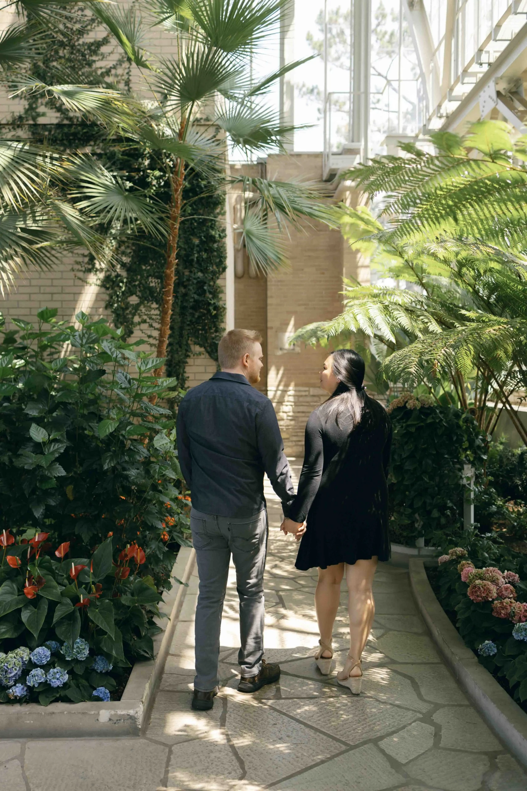 An engaged couple walking hand in hand in a historic greenhouse in Saint Louis, Missouri, shot by Stacey Vandas Photography.