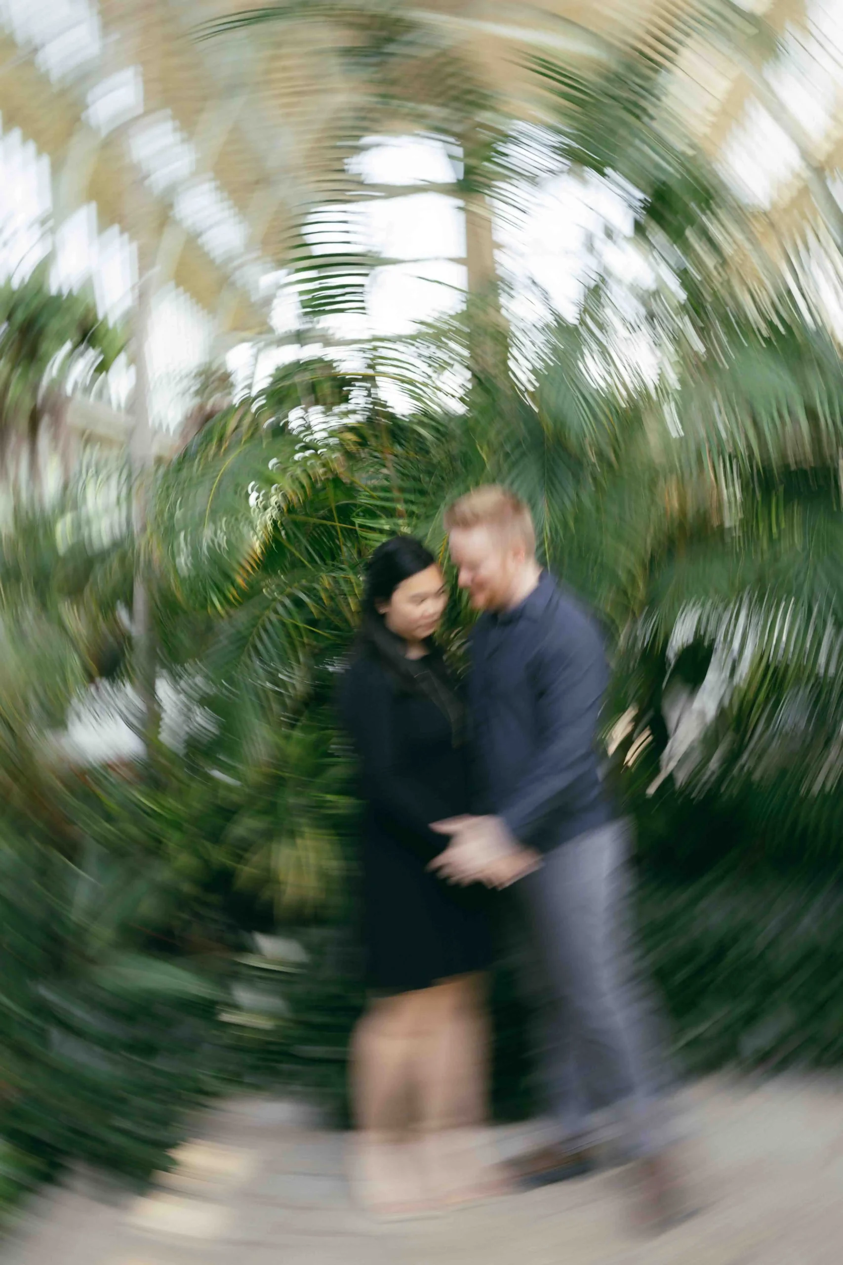 An engaged couple in a greenhouse shot with a motion blur photography style.