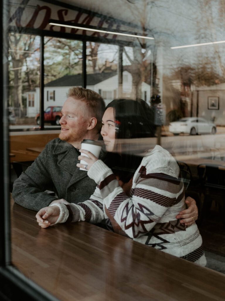 A couple drinking coffee in a coffee shop window with a moody brown aesthetic, shot by Stacey Vandas.