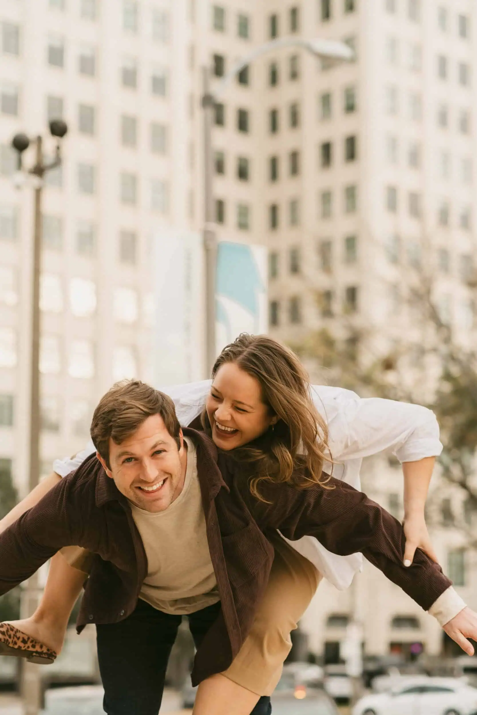 A couple laughing in a piggyback ride pose in downtown St. Louis, Missouri with an urban, filmy aesthetic.