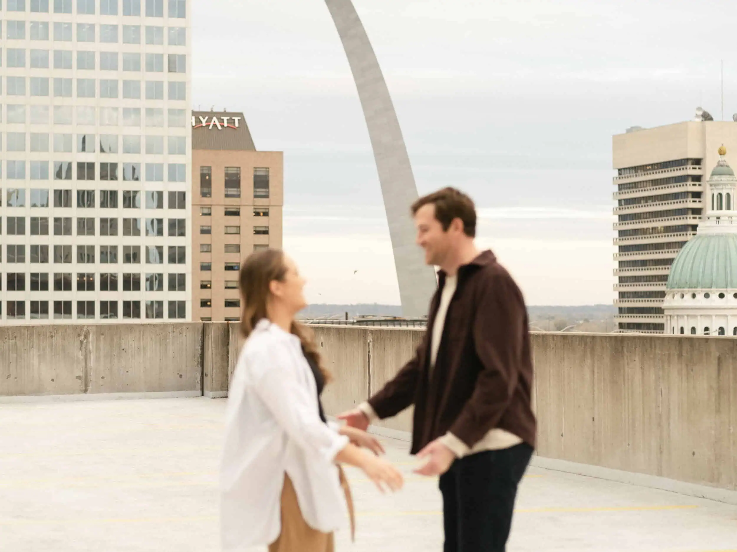 A couple laughing on an urban rooftop in Downtown Saint Louis, Missouri with the Arch in the background, shot with a documentary style by Stacey Vandas Photography.