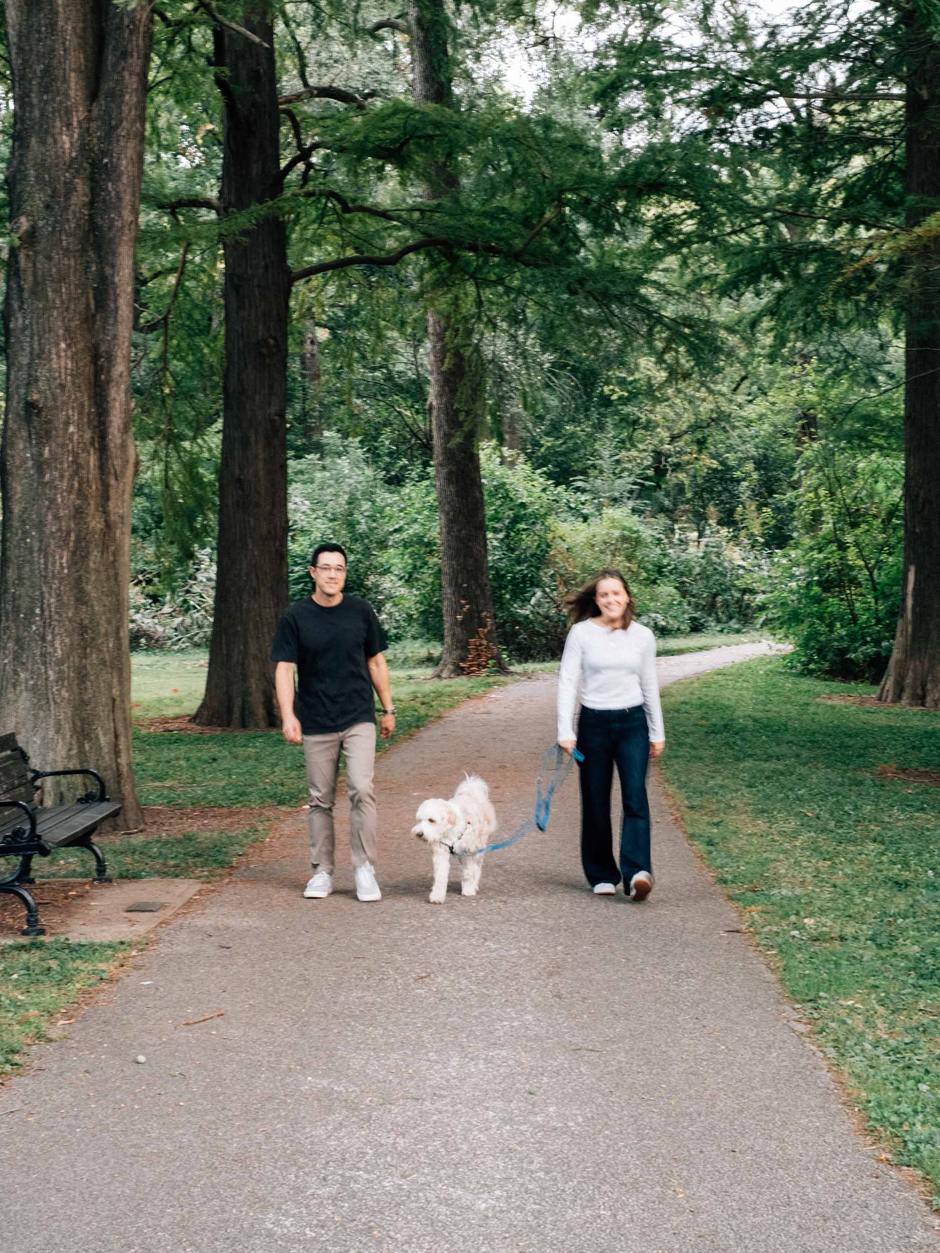 A couple and their dog walking down a path with tall trees, with a nostalgic film photography style.