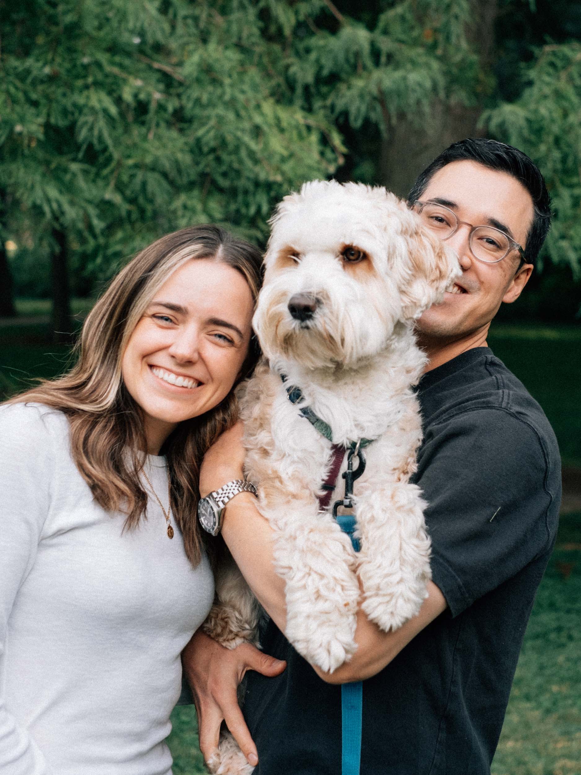A couple holding their Tibetan terrier puppy and smiling at the camera in a film photography style.