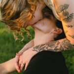 a woman leans over a sitting man and kisses him upside down in golden hour light