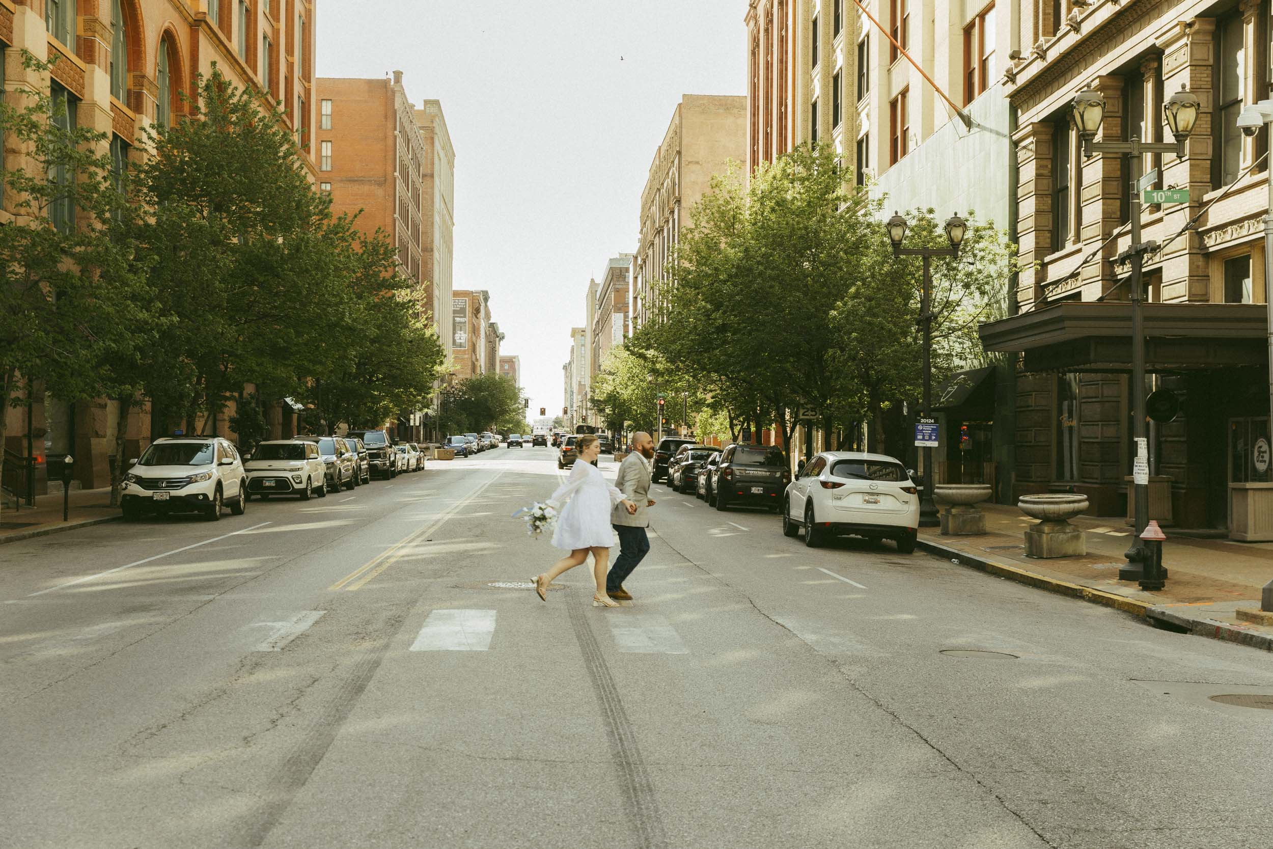 A couple runs across a downtown street during an urban elopement in St. Louis, Missouri