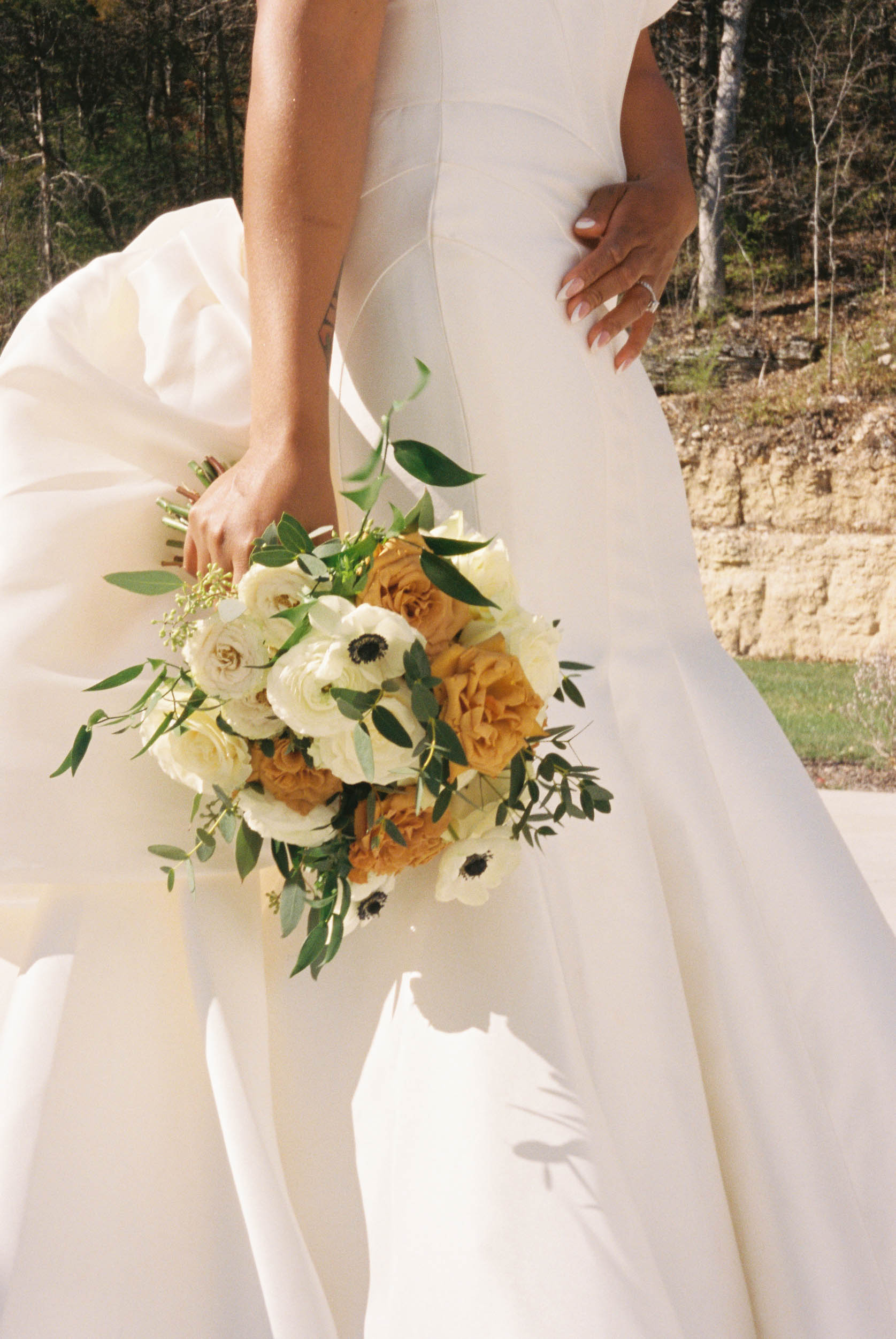 A film wedding photography close-up of a bride holding her bouquet in front of her dress.