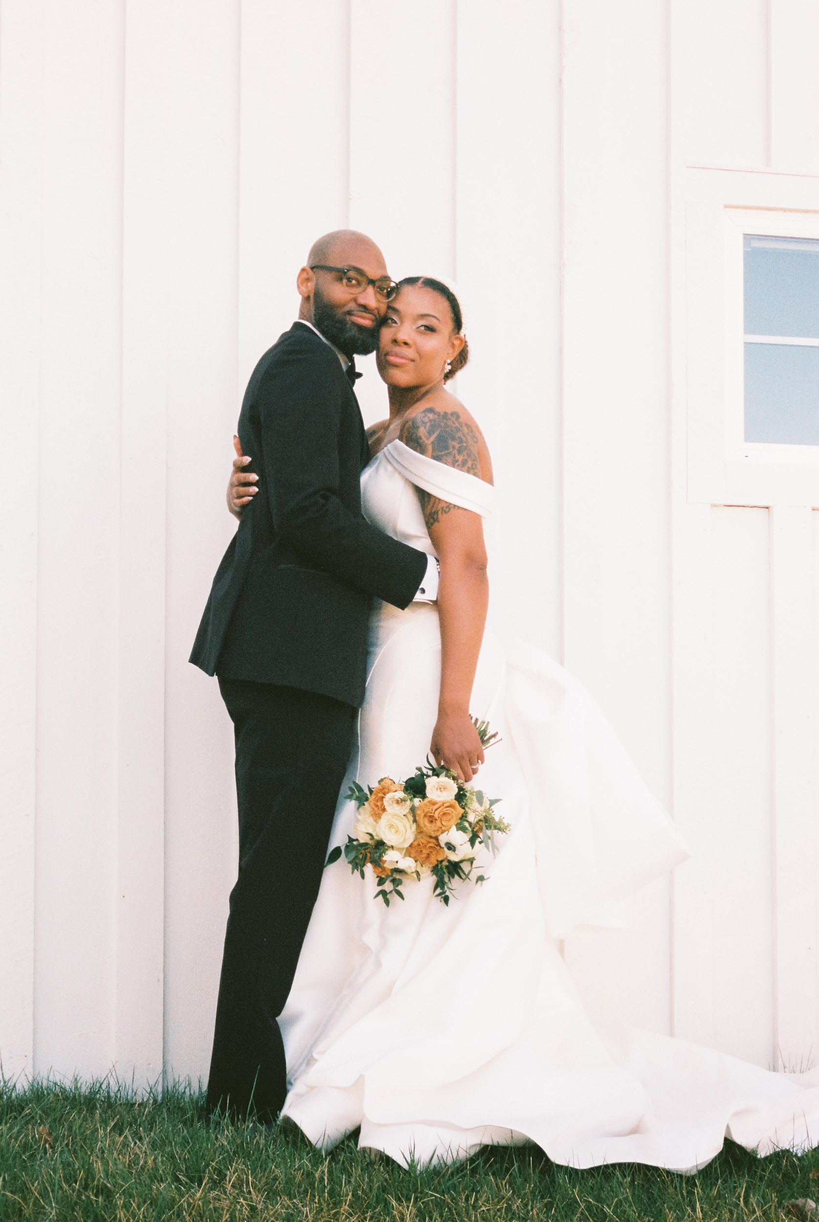 Film wedding photography of a bride and broom posing in front of a white barn.