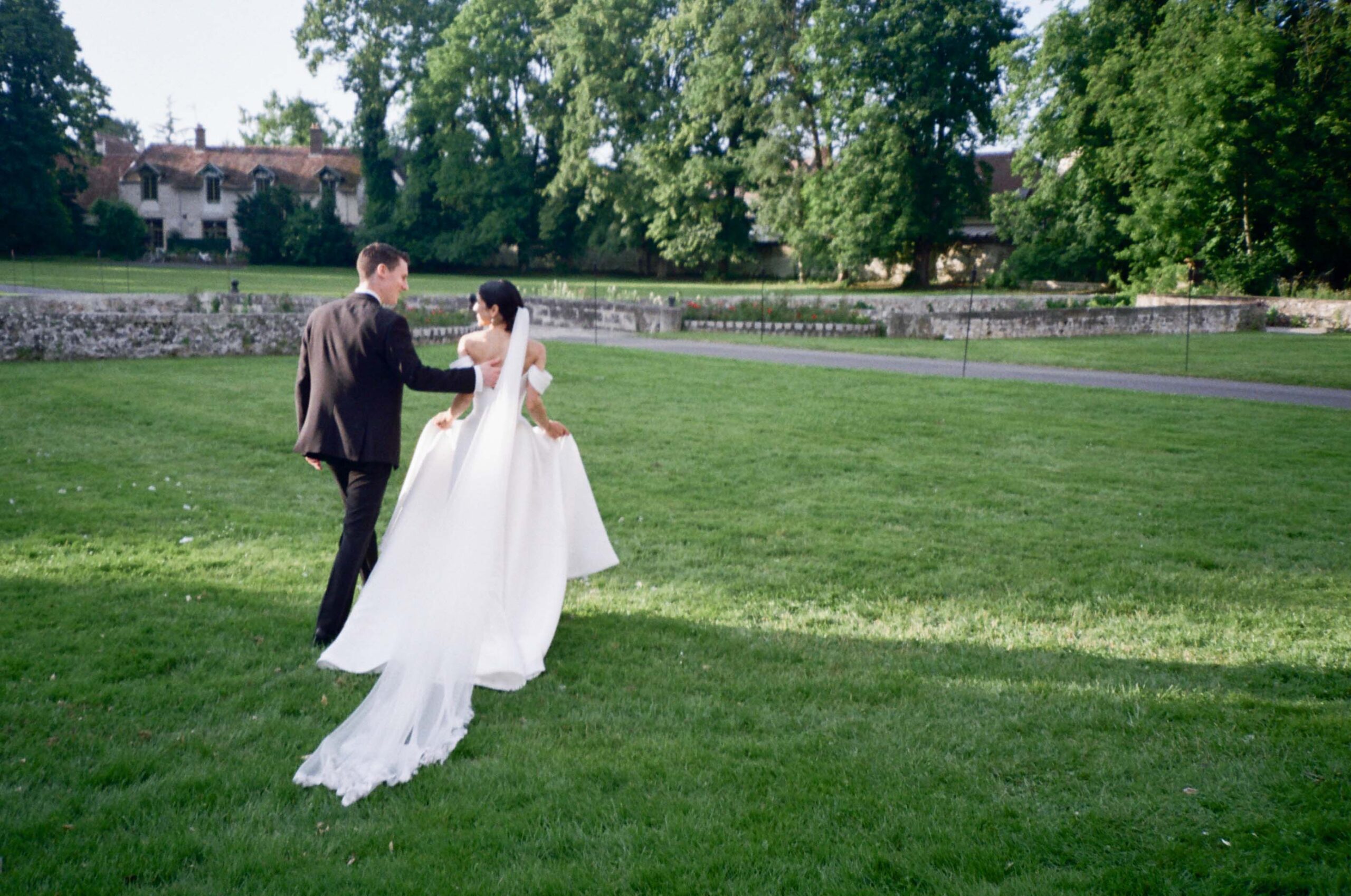 A bride and groom walk through a lawn on their wedding day, shot in a documentary-style with 35mm film by Stacey Vandas Photography.