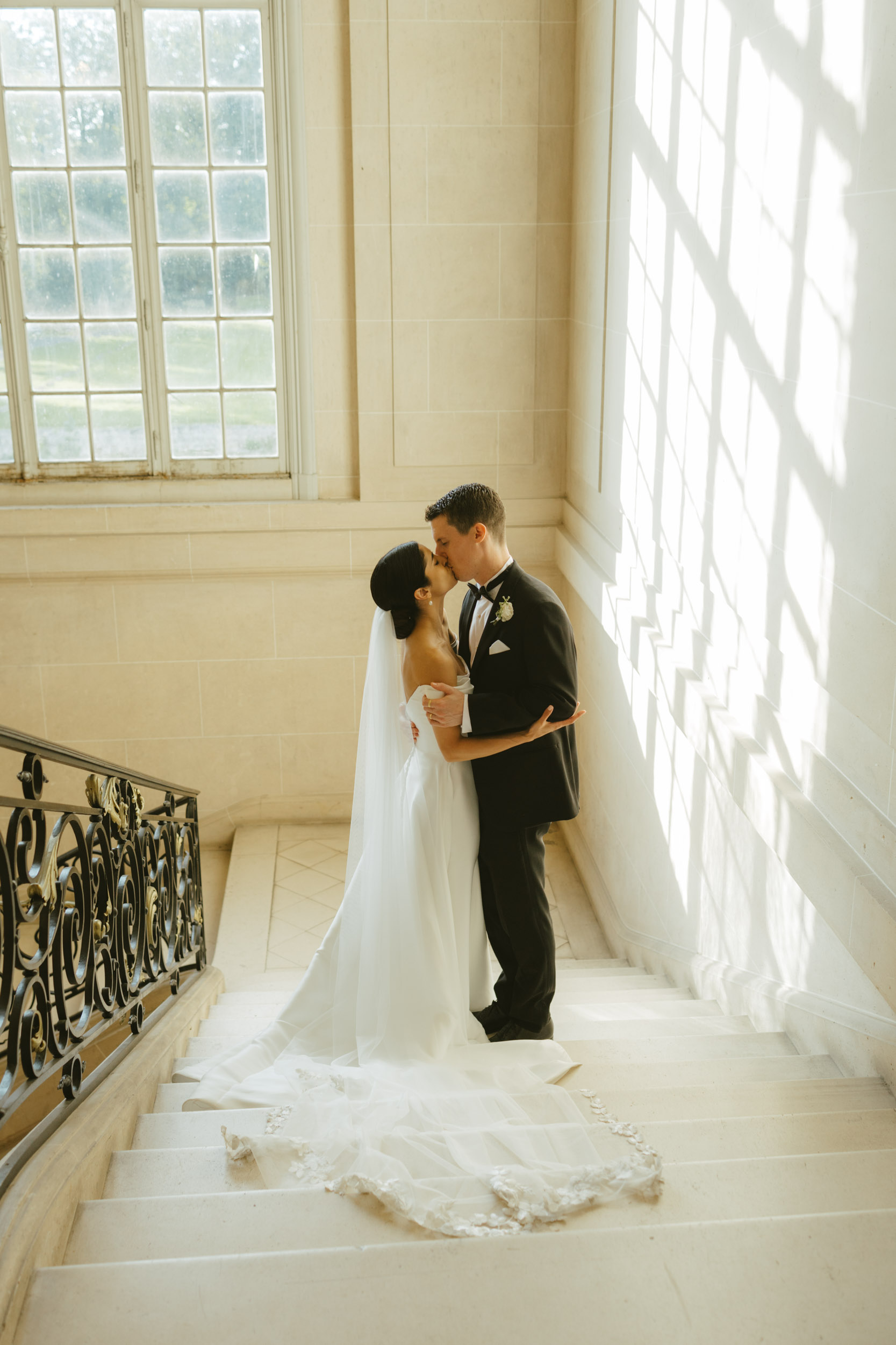 A bride and groom kiss on the stairs of a historic chateau in an editorial wedding photo.