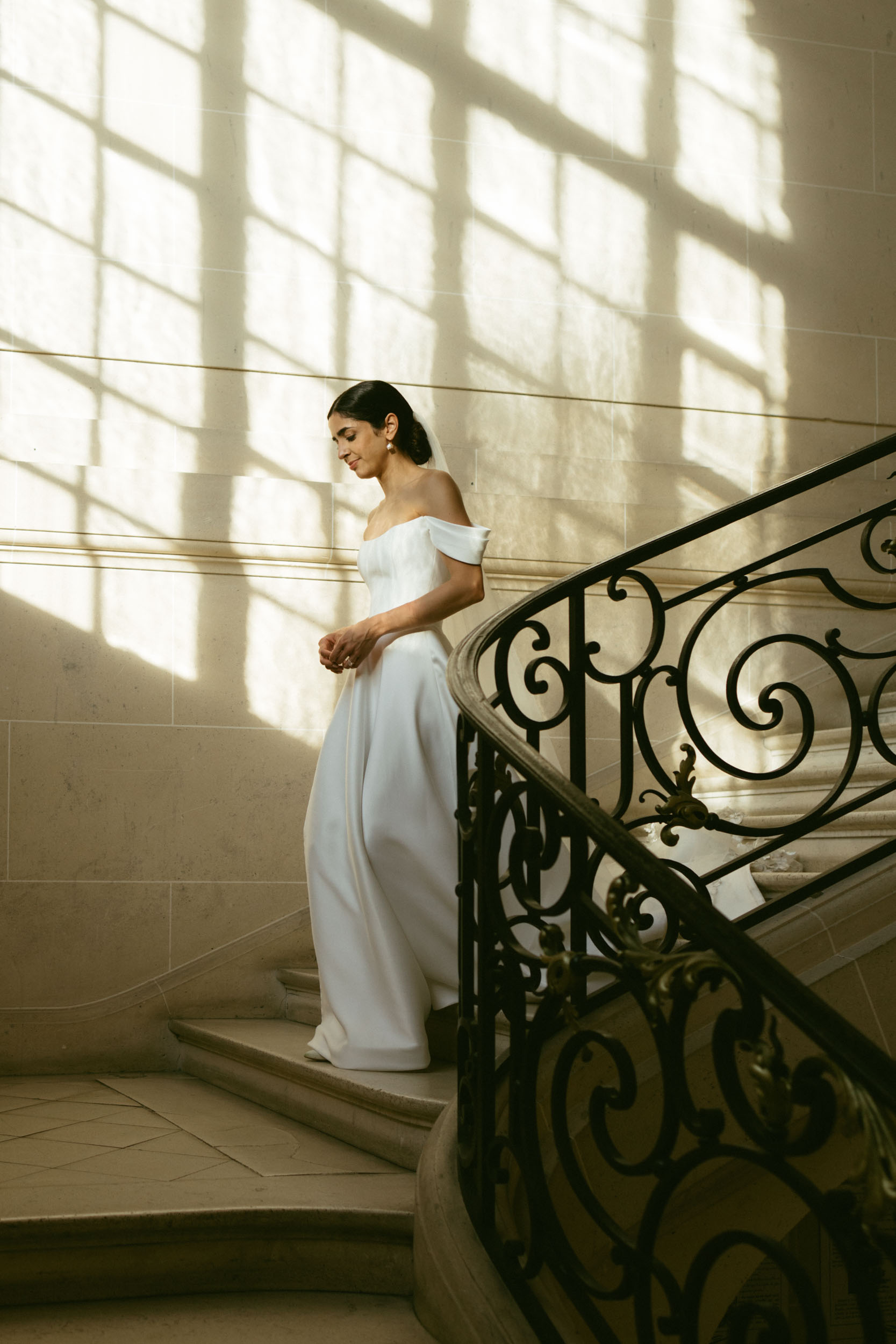 A bride walks down the stairs with shadows from windows in an editorial wedding photography photoshoot.