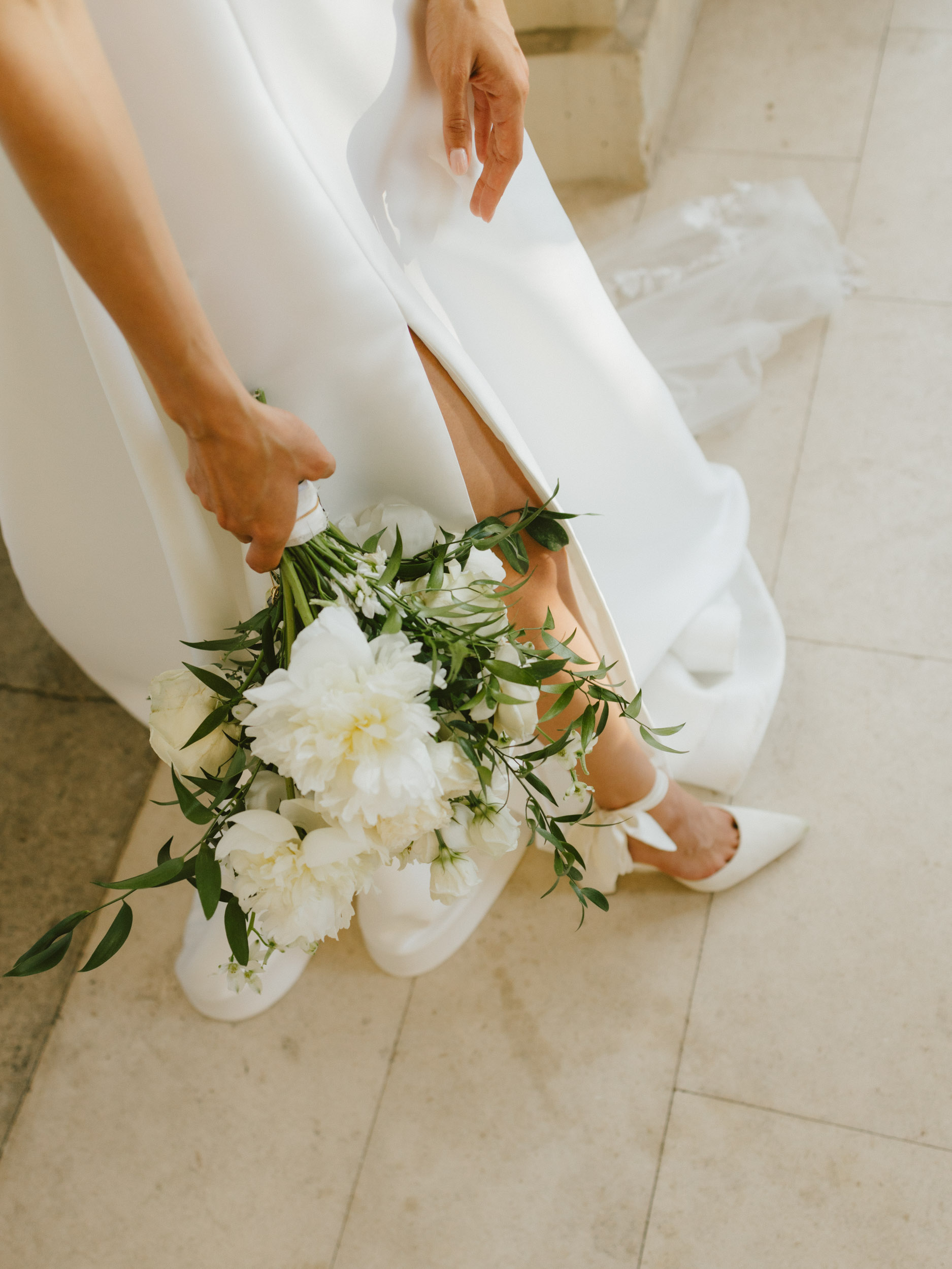 A close-up of a bridal bouquet and shoes in an editorial photography style.