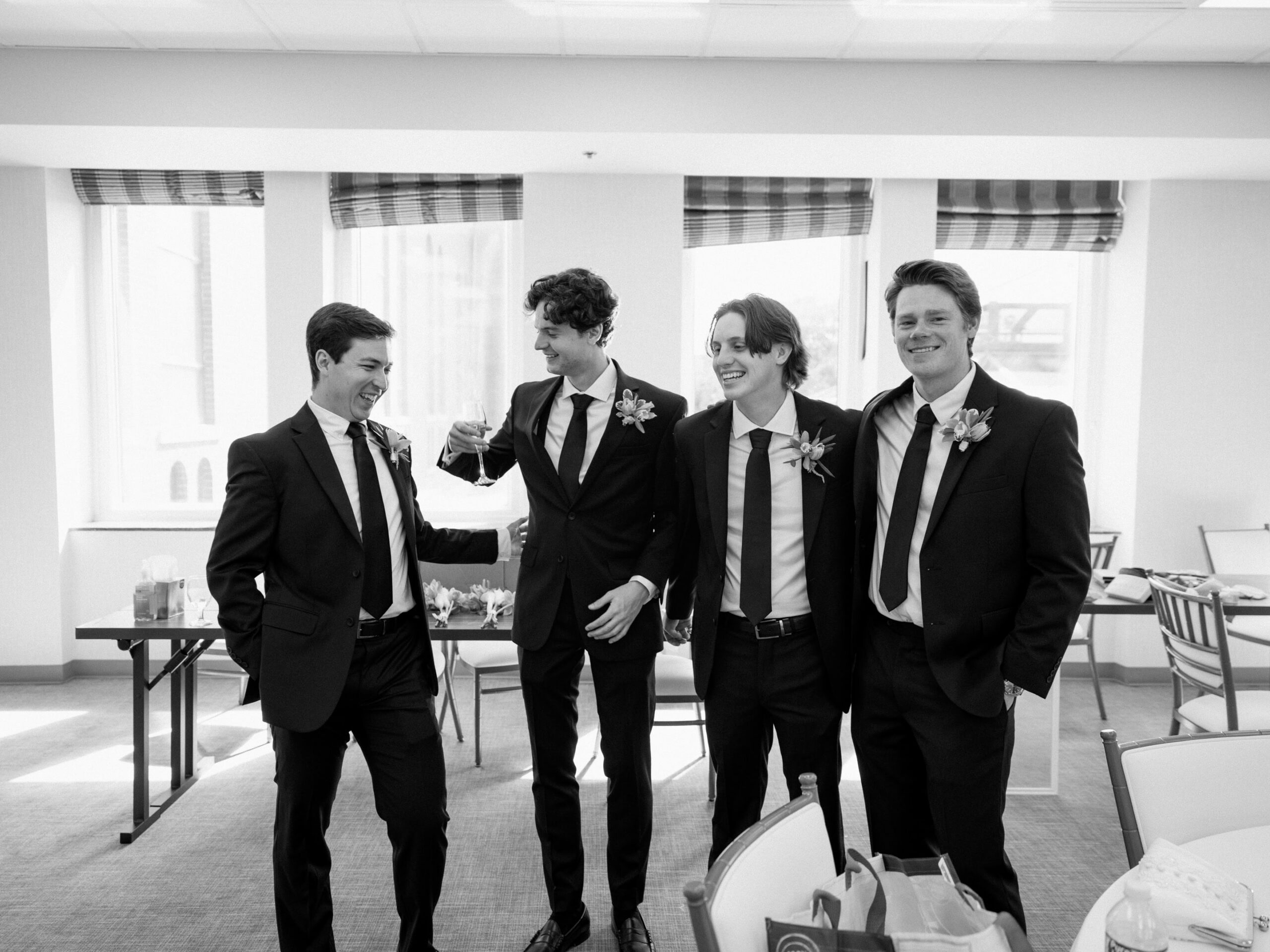 A group of groomsmen laugh in a black and white photo.