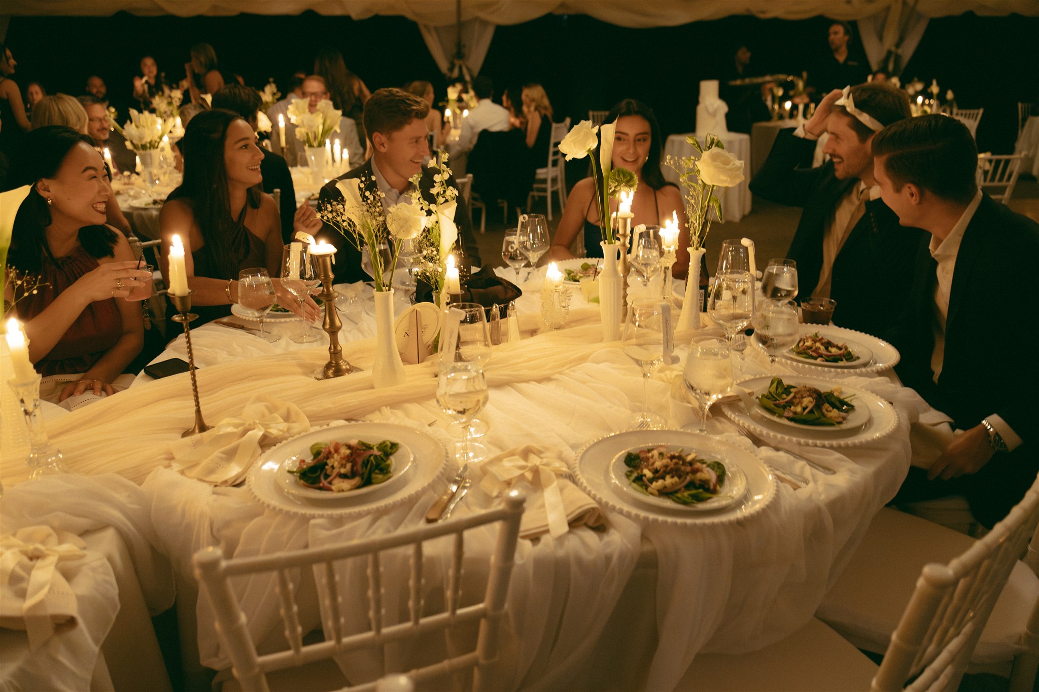 An ambient photo at a wedding reception of a table of guests laughing in candelight, shot in a documentary style.