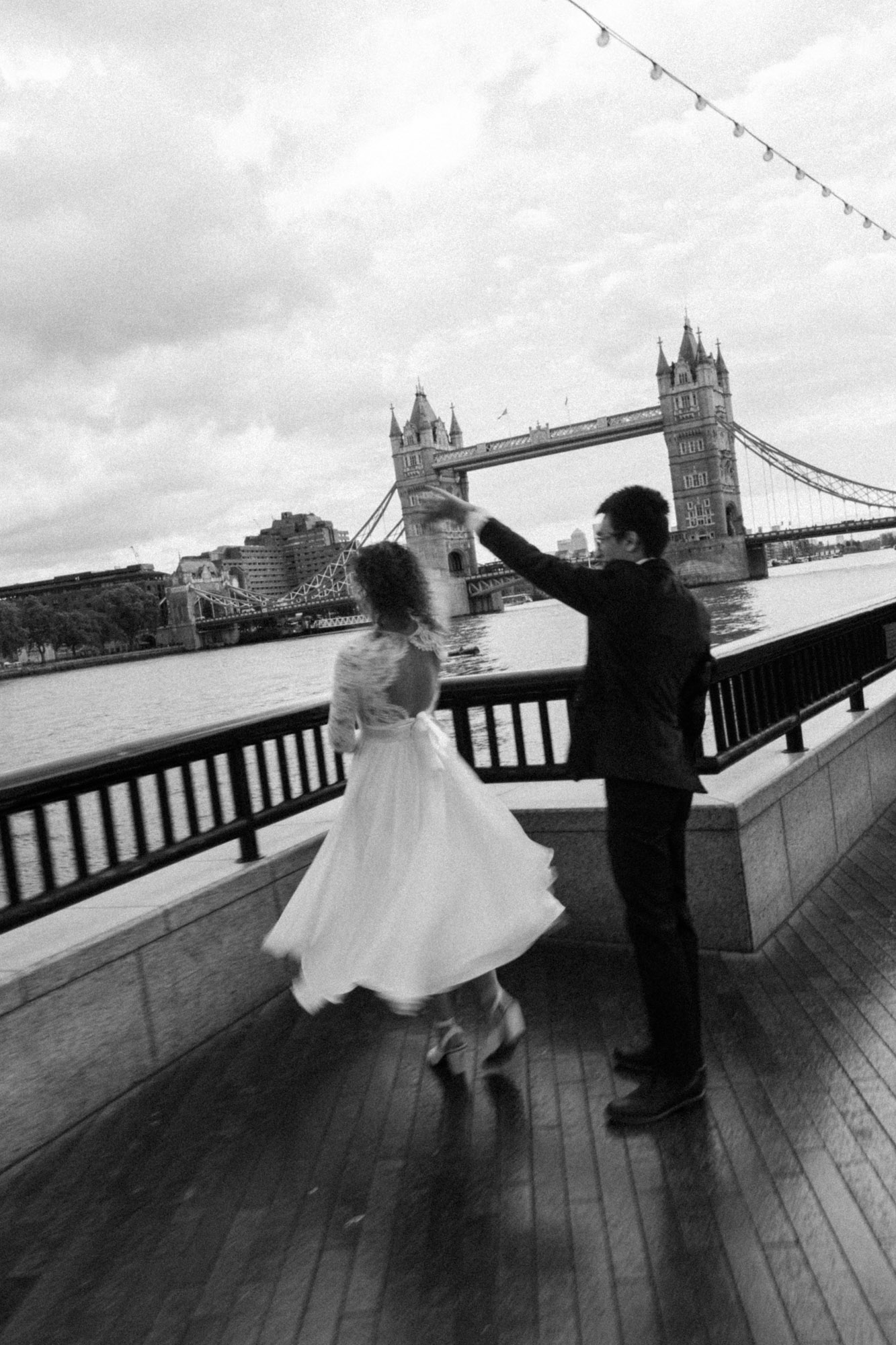 A black and white photo of a couple dancing on the Thames during a London elopement, shot with a filmy, documentary style by Stacey Vandas Photography.