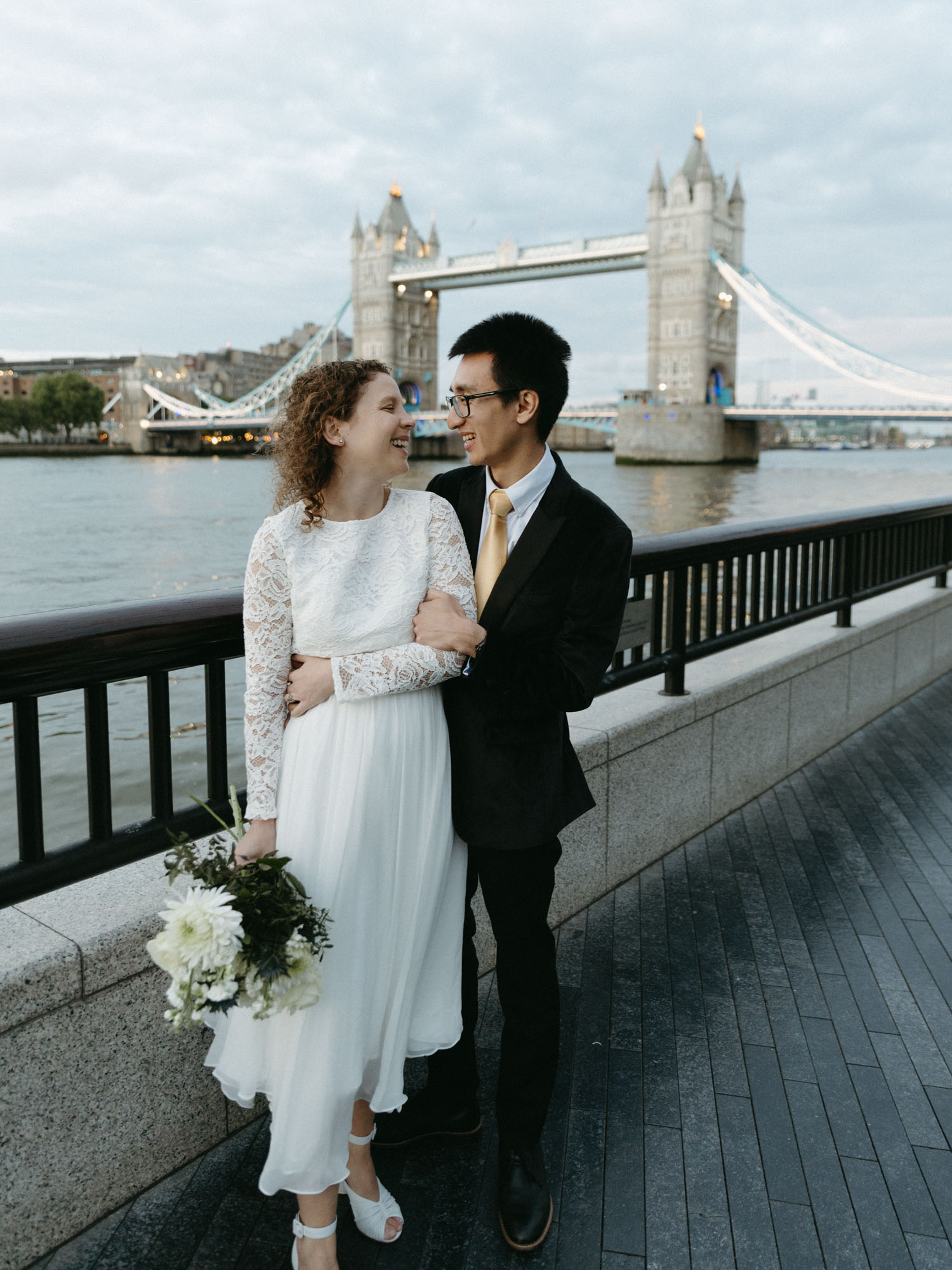 An eloping couple smiles at each other with Tower Bridge and the River Thames in the background.