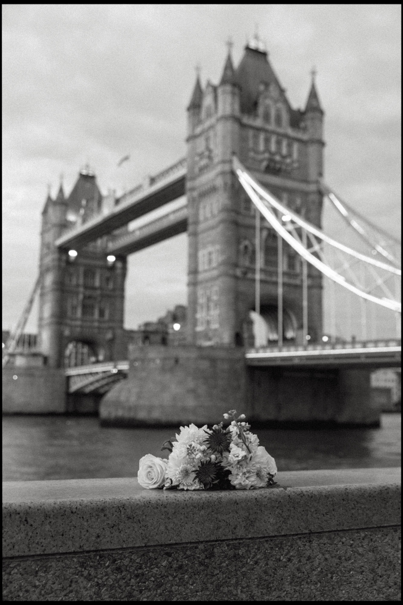 A black and white photo of a bridal bouquet with the Tower Bridge in the background.