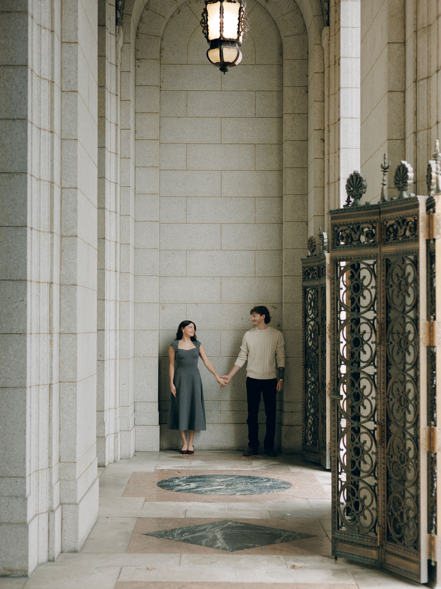 A couple hold hands under an arched entry for a historic library.