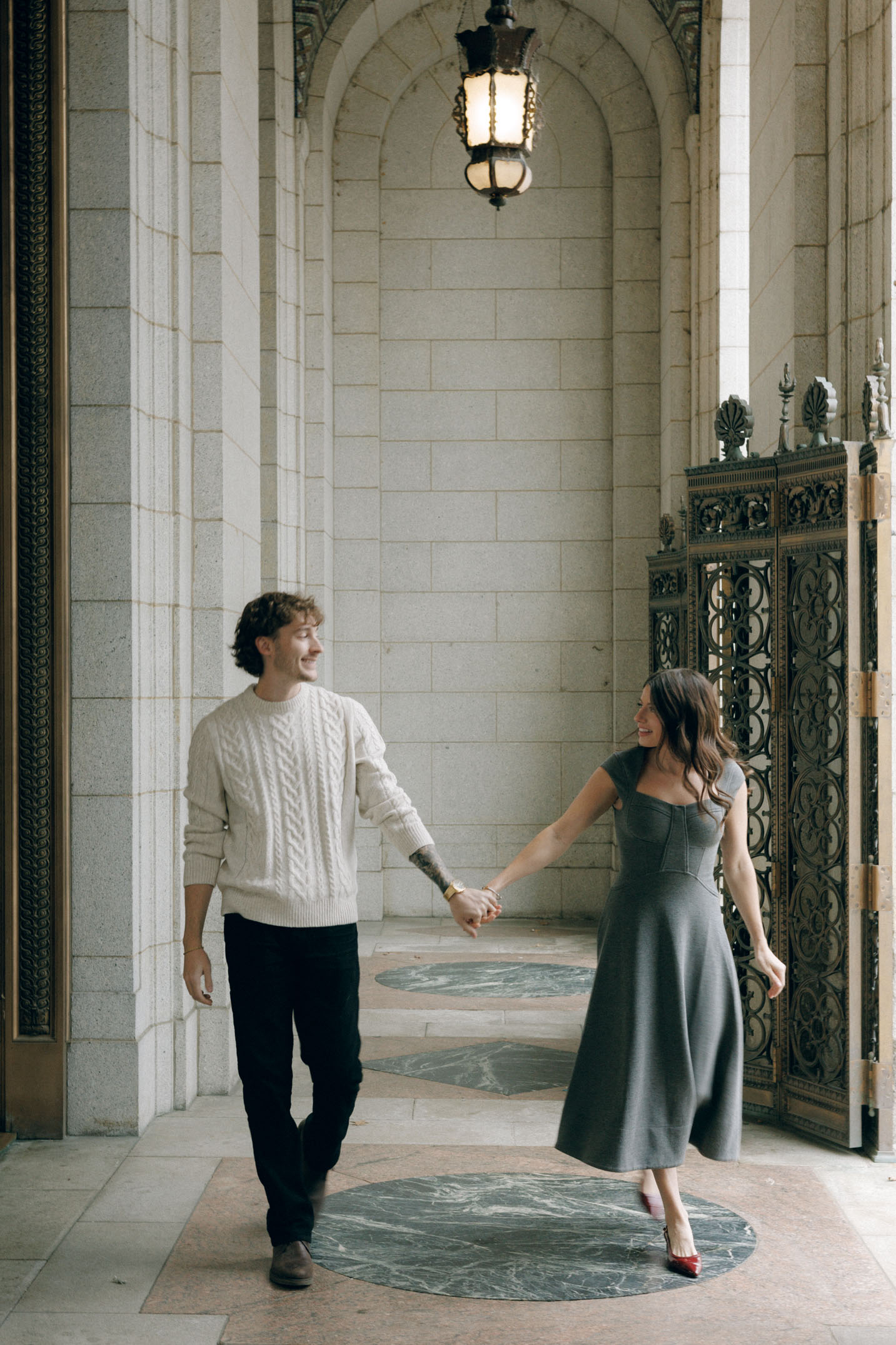 A couple walks holding hands in a historic building.