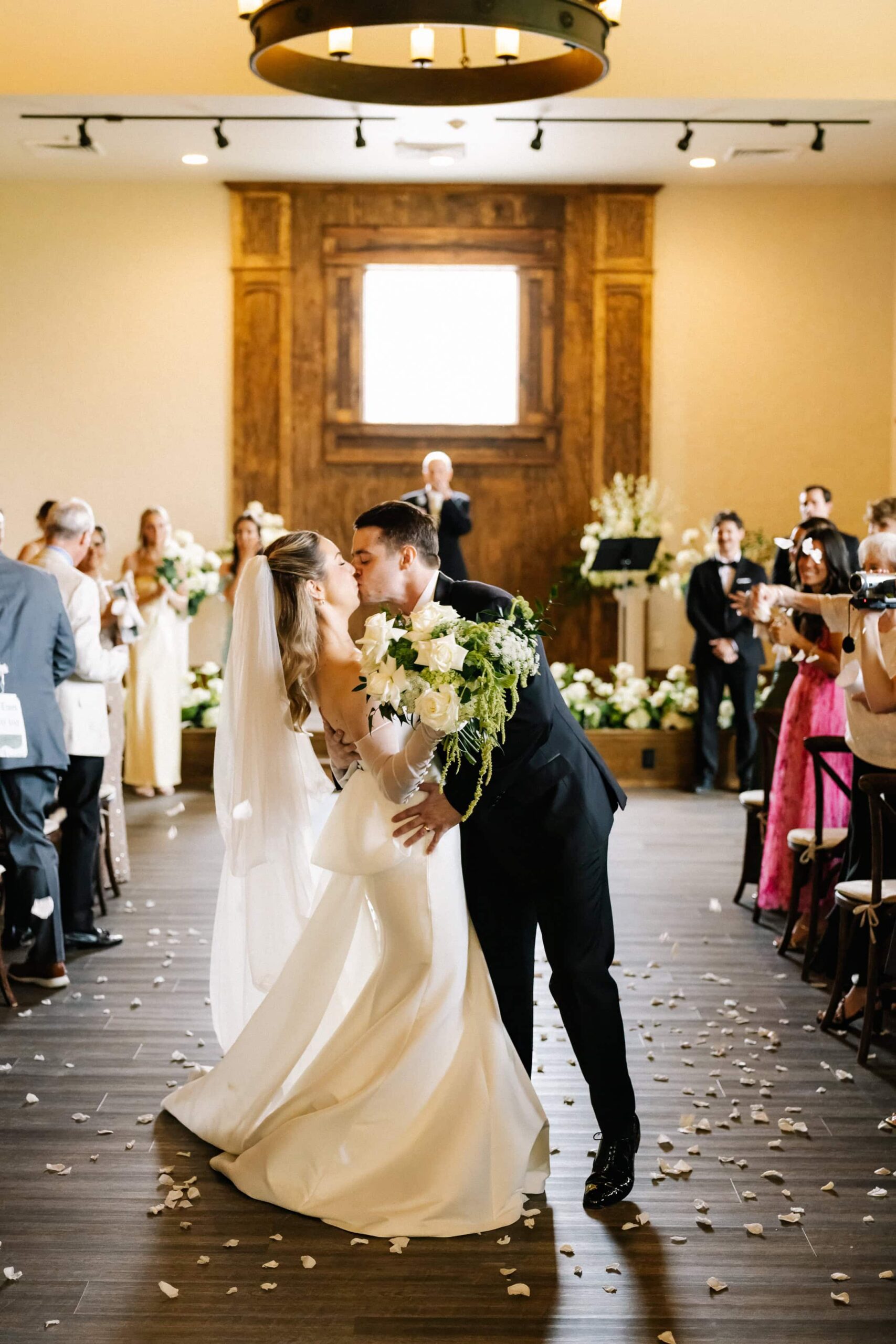 A bride and groom share a kiss in the aisle.