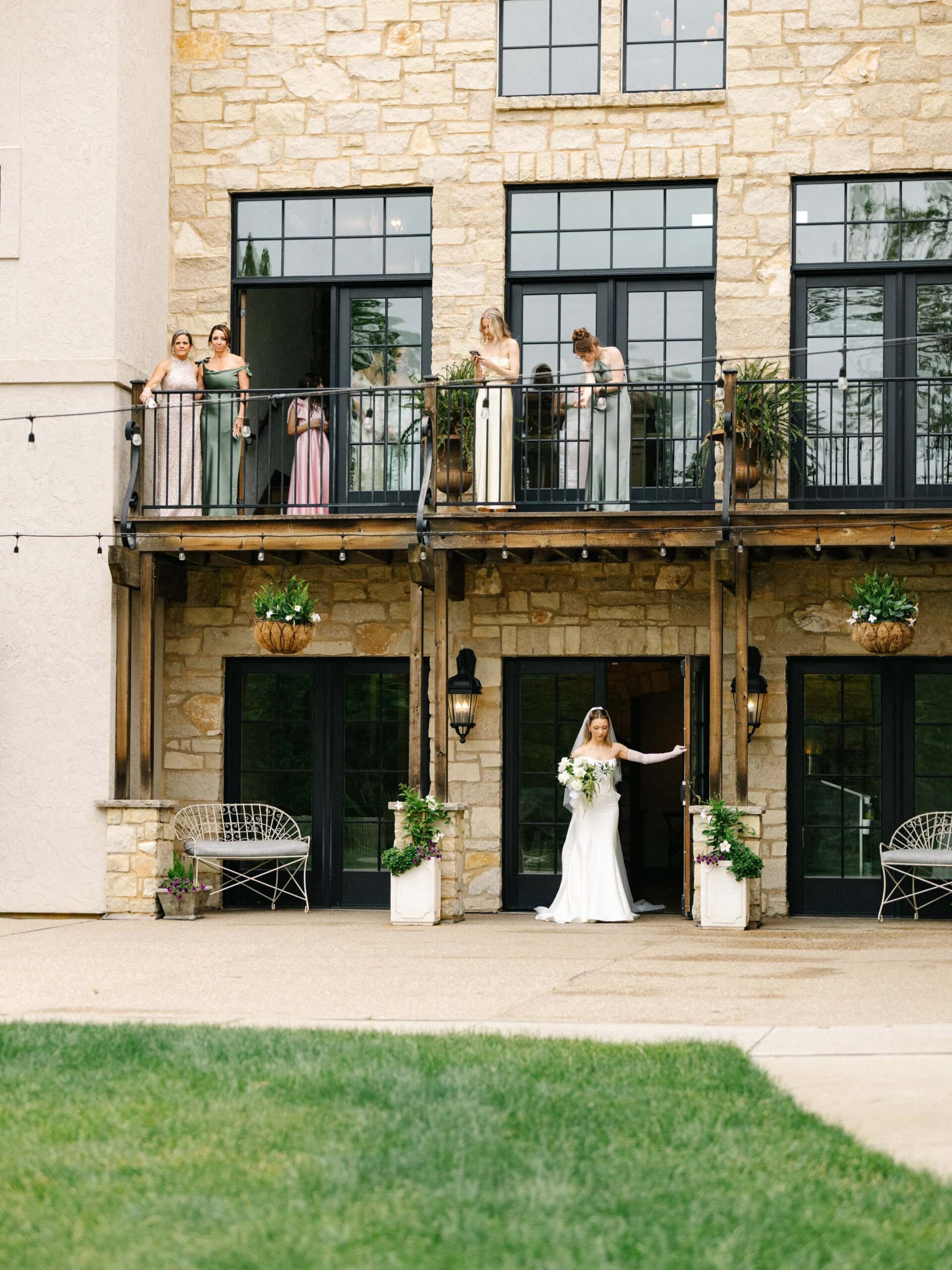 A bride prepares for her first look with the groom and guests on the balcony above look on.