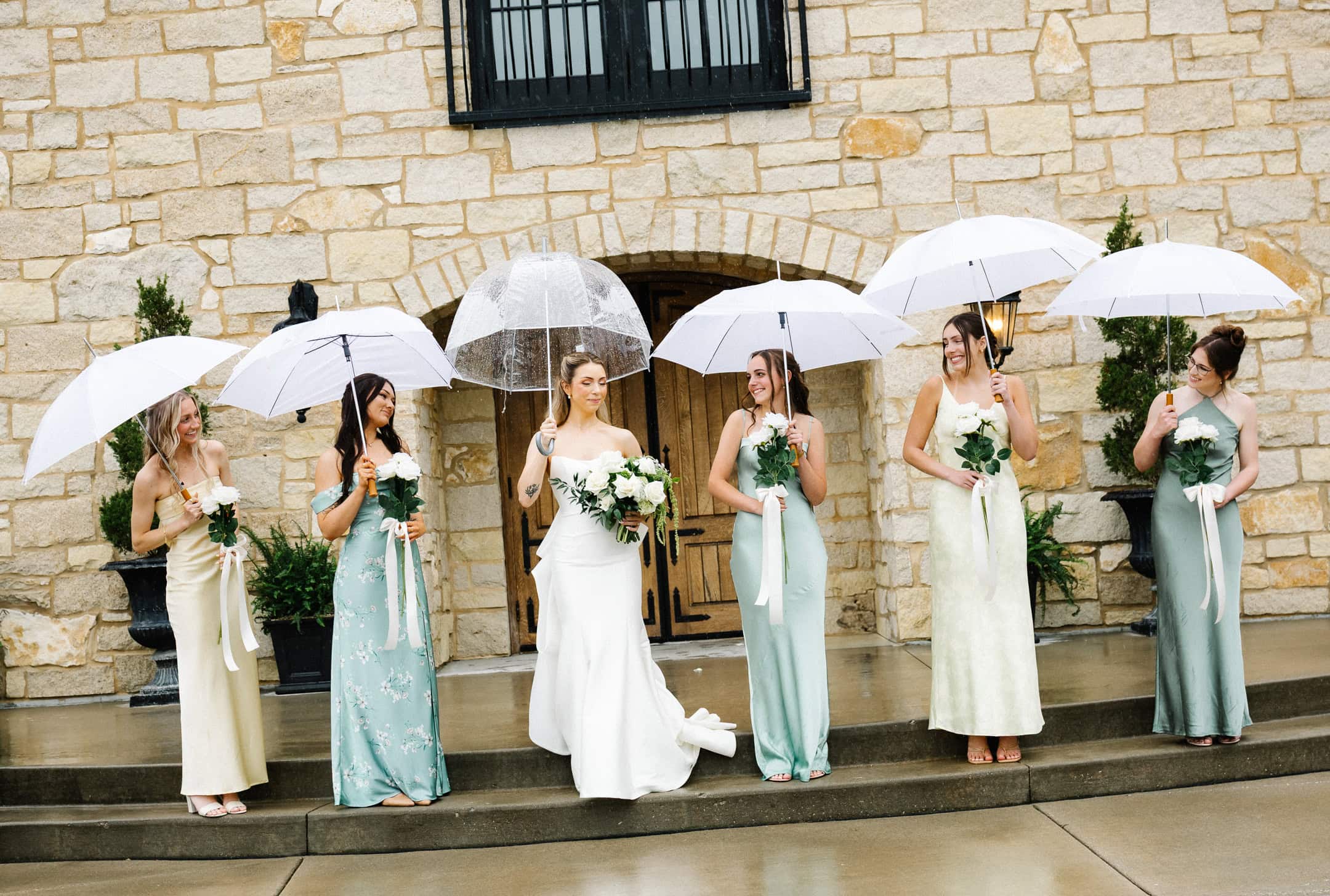 A bride and bridesmaids standing with umbrellas on a rainy wedding day.