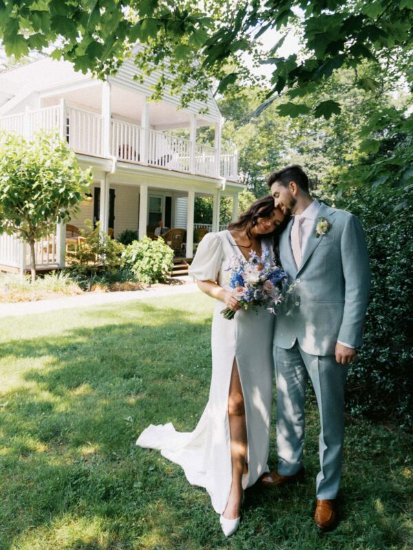 Bride and groom embrace under shady trees in a backyard wedding.