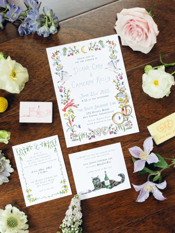 Floral-themed wedding invitations and cards are arranged on a wooden floor, surrounded by pastel flowers and illustrated matchboxes.