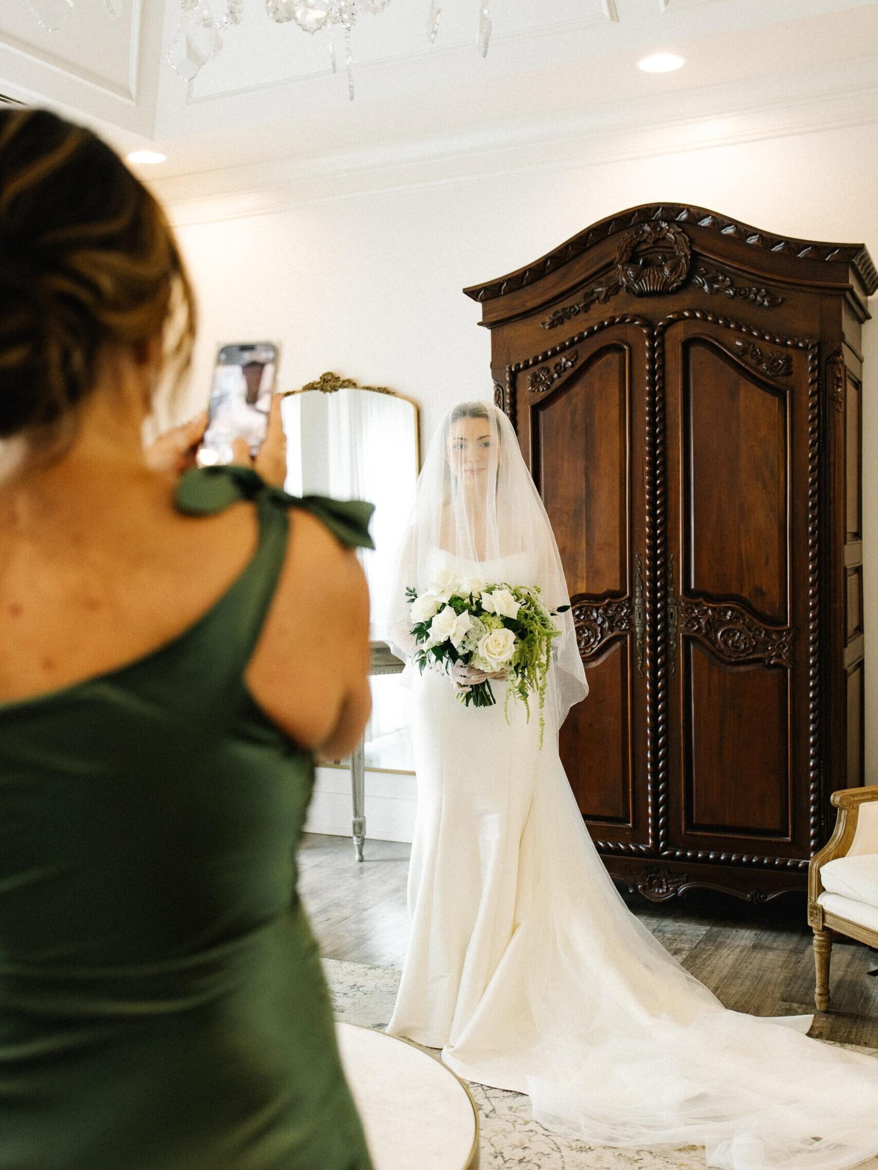 bride posing for her mom's photo in her veil with her bouquet.