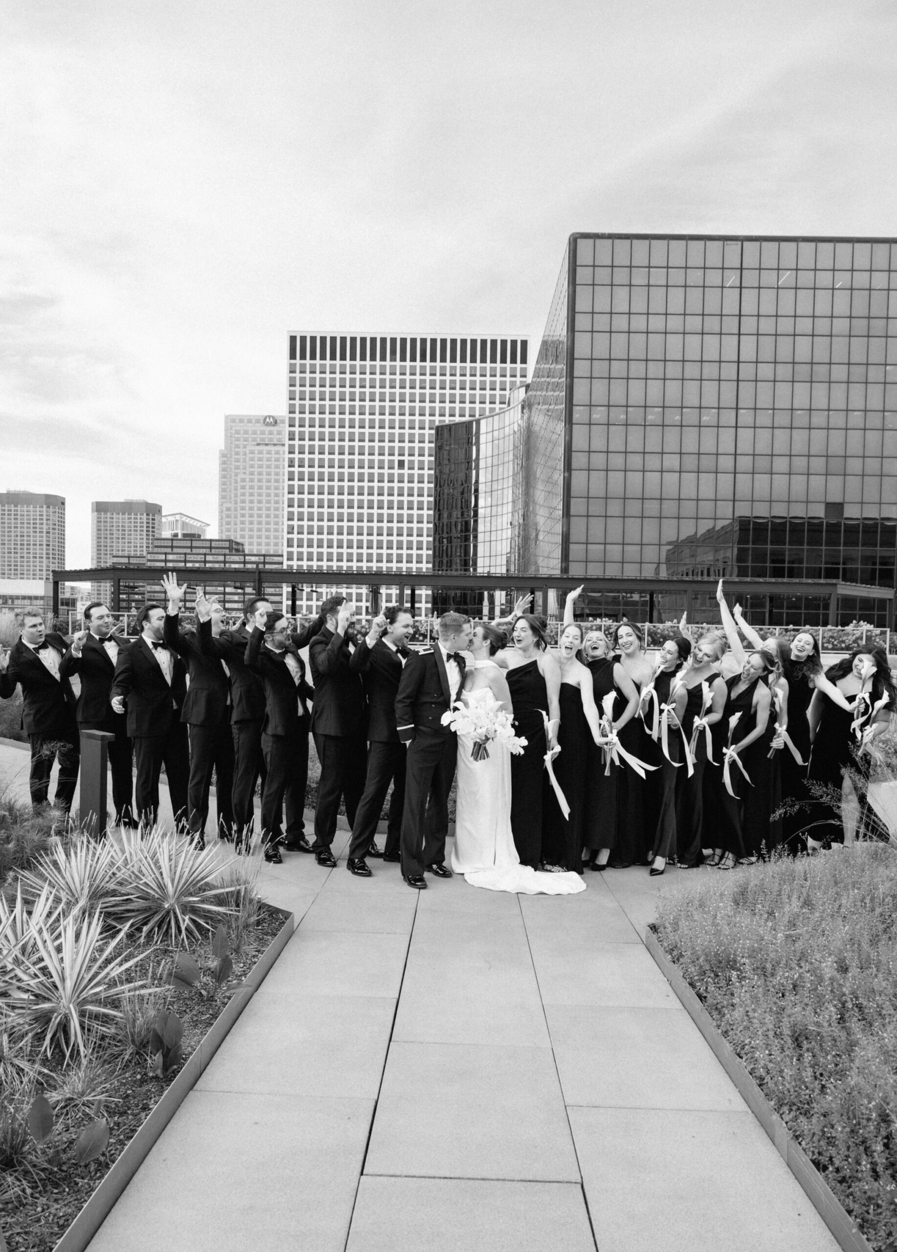 A couple kisses as their bridal party cheers in a black and white photo on a Chicago rooftop wedding.