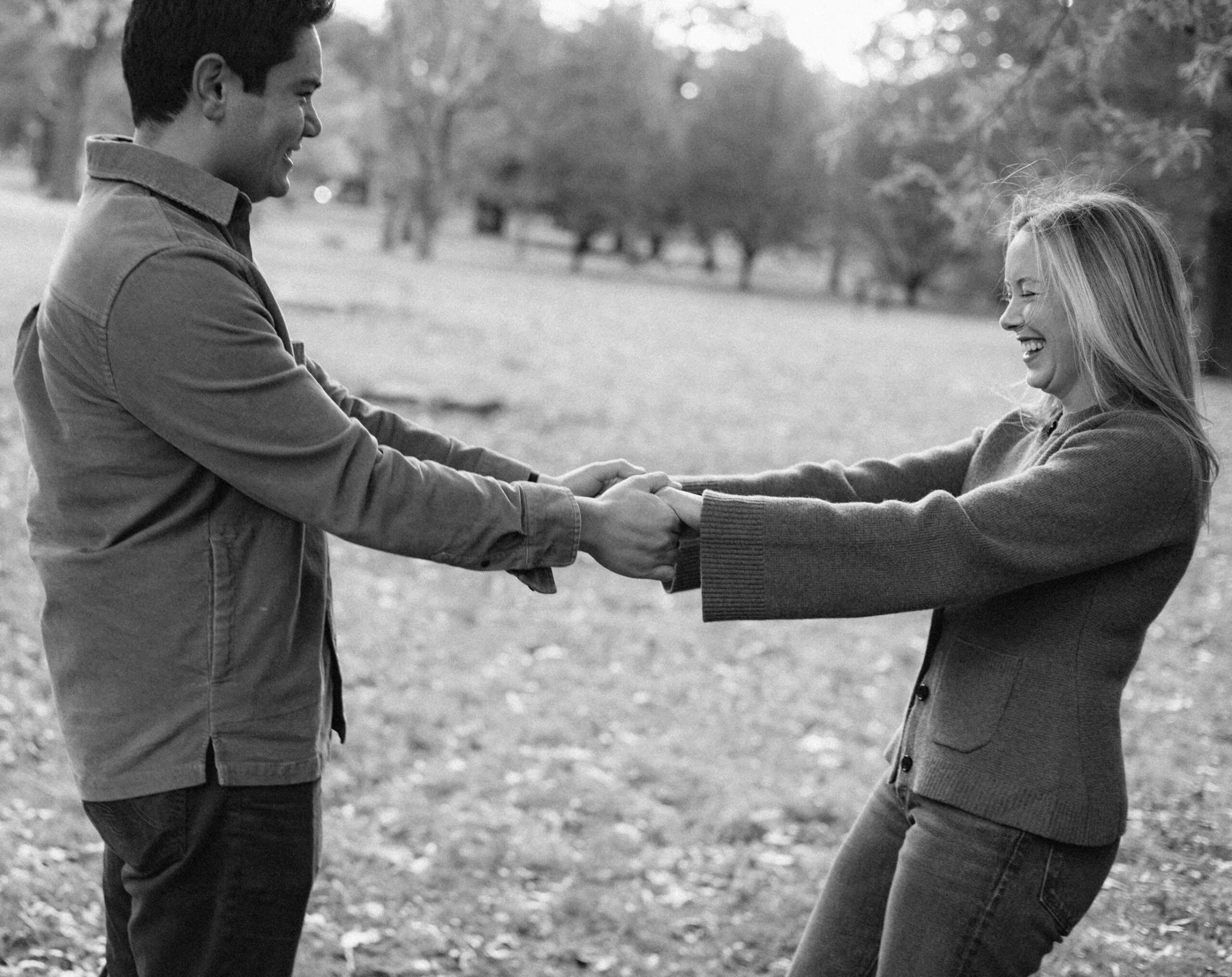 A couple holds hands in a park in a black and white fall engagement photo.