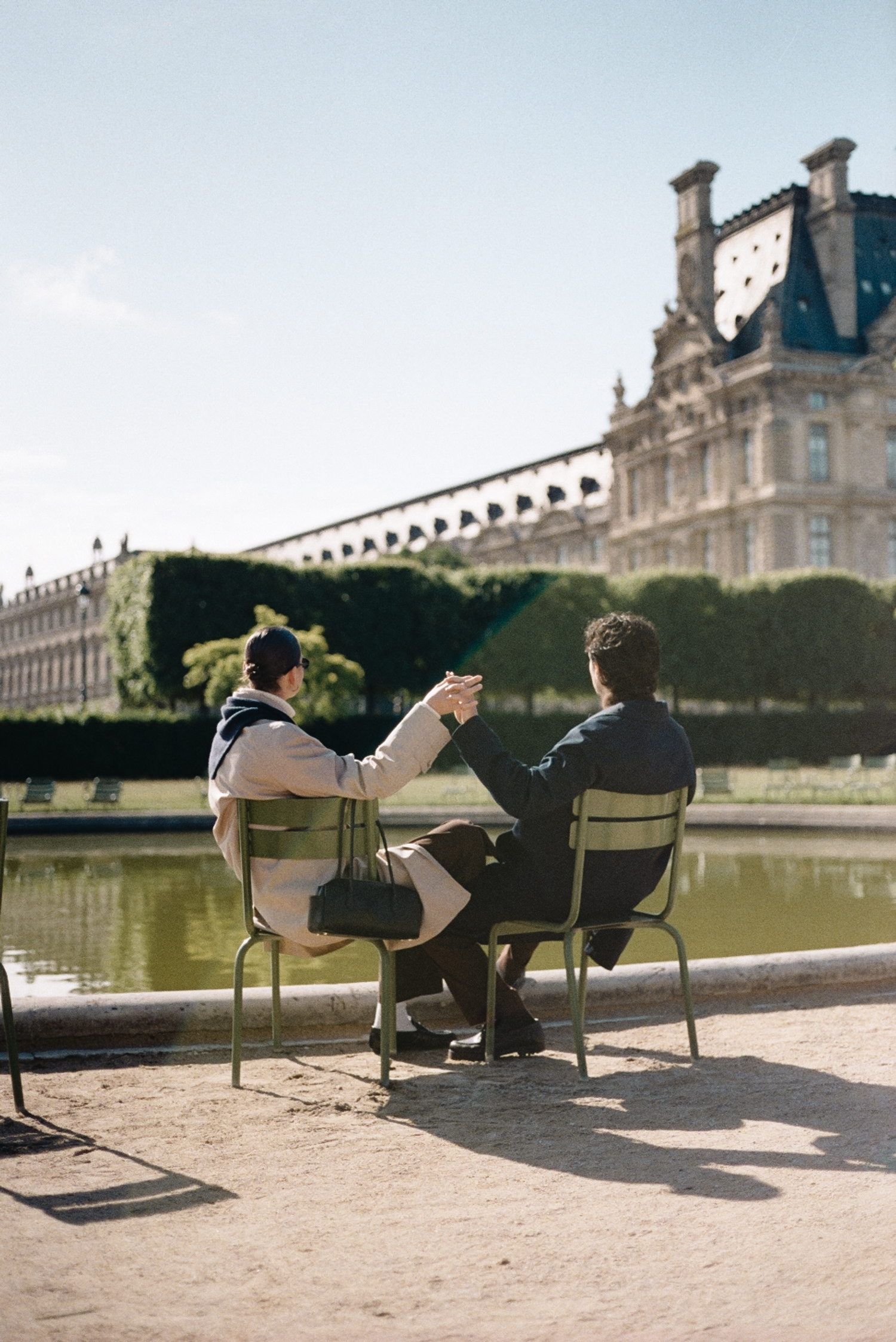 Two people sitting on chairs by a pond with a historic building in background.