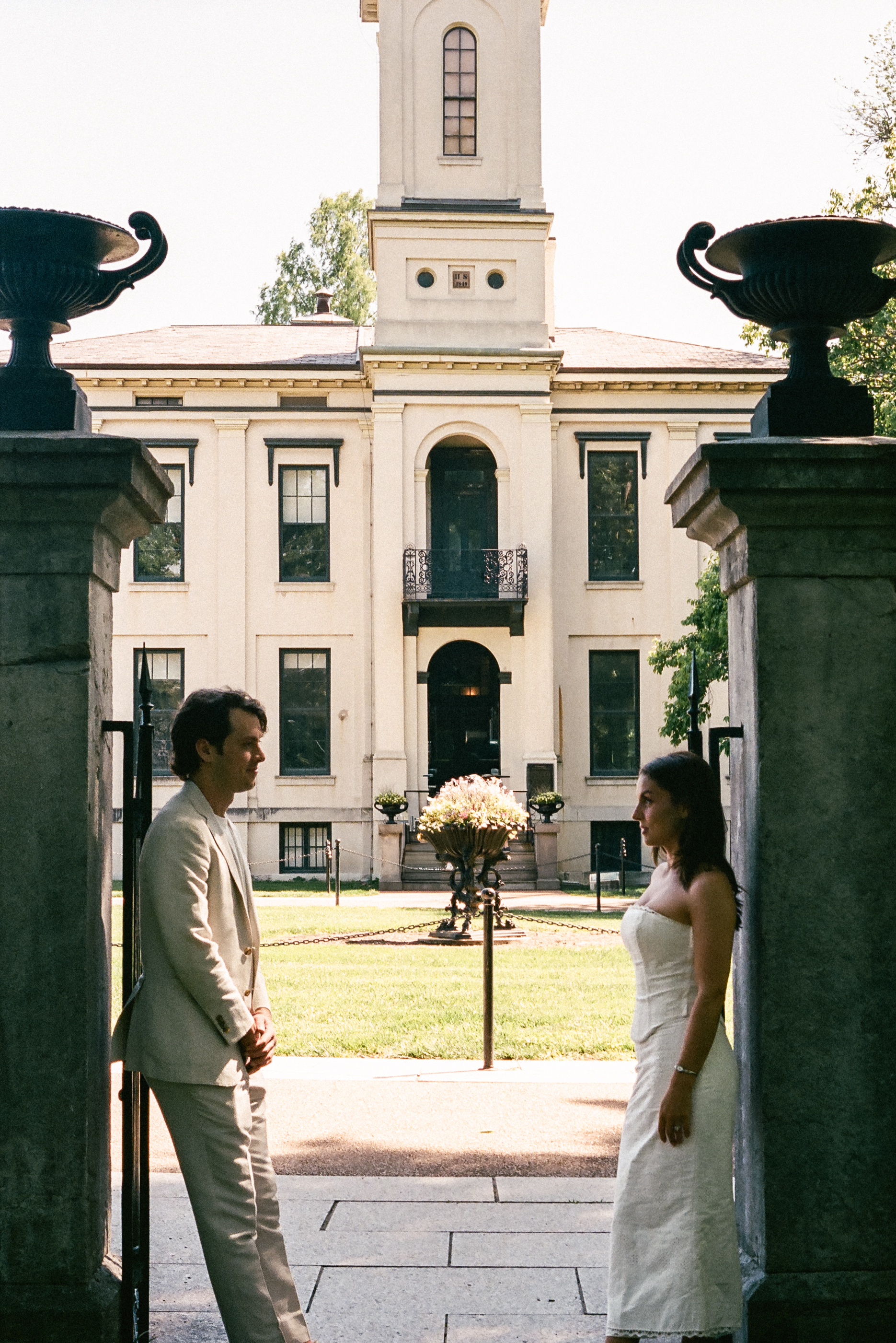 couple leaning against gates of a historic house in an engagement photo on film